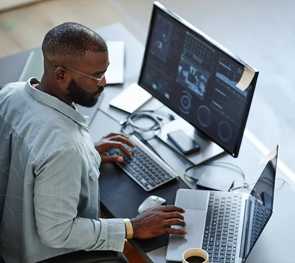 Busy man looking at potential hires on desktop computer and laptop