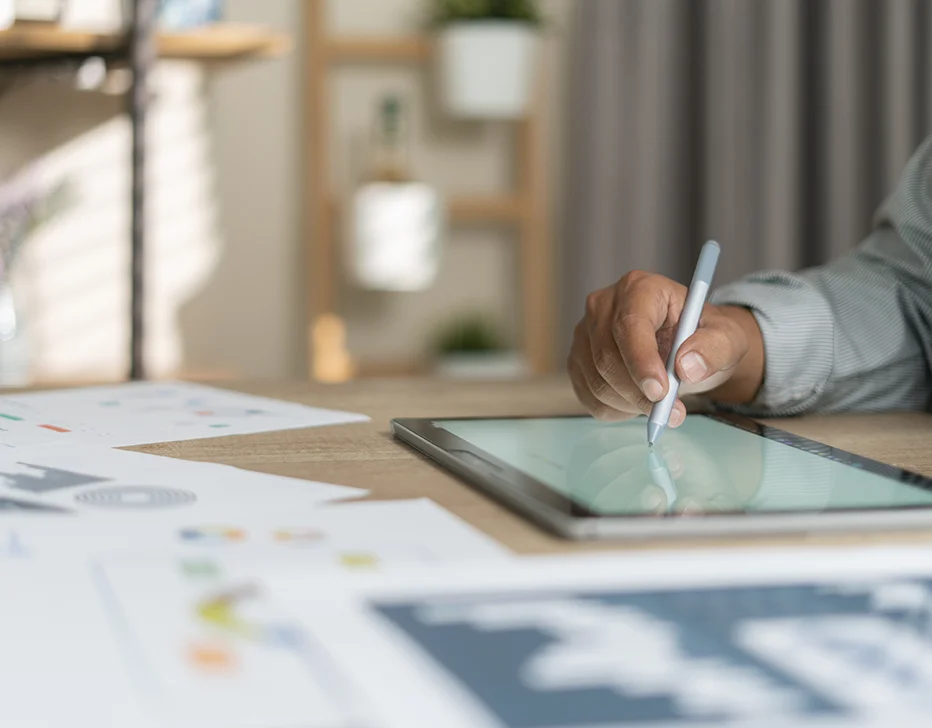 Someone writing something on a mobile tablet with lots of diagram papers on the table.