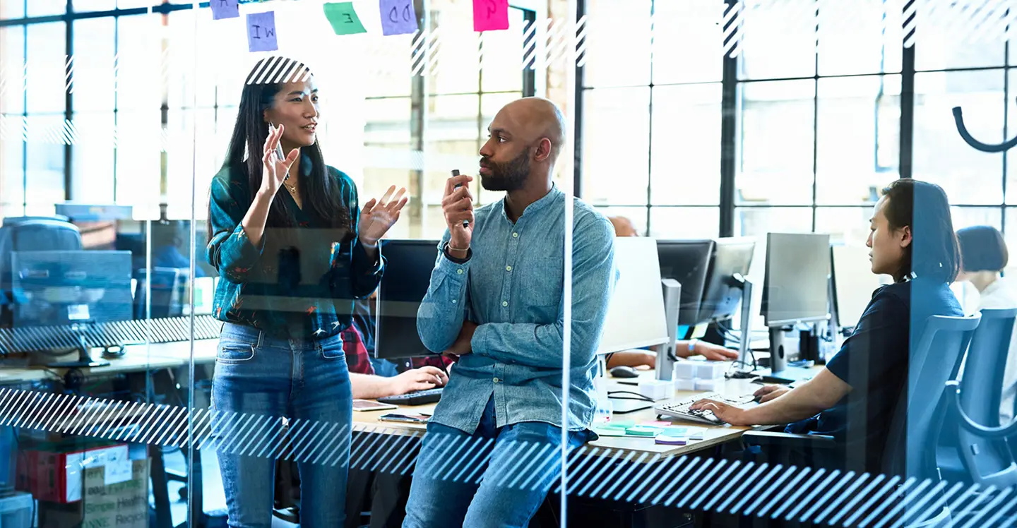 Man and woman discussing in office with people working in the background.
