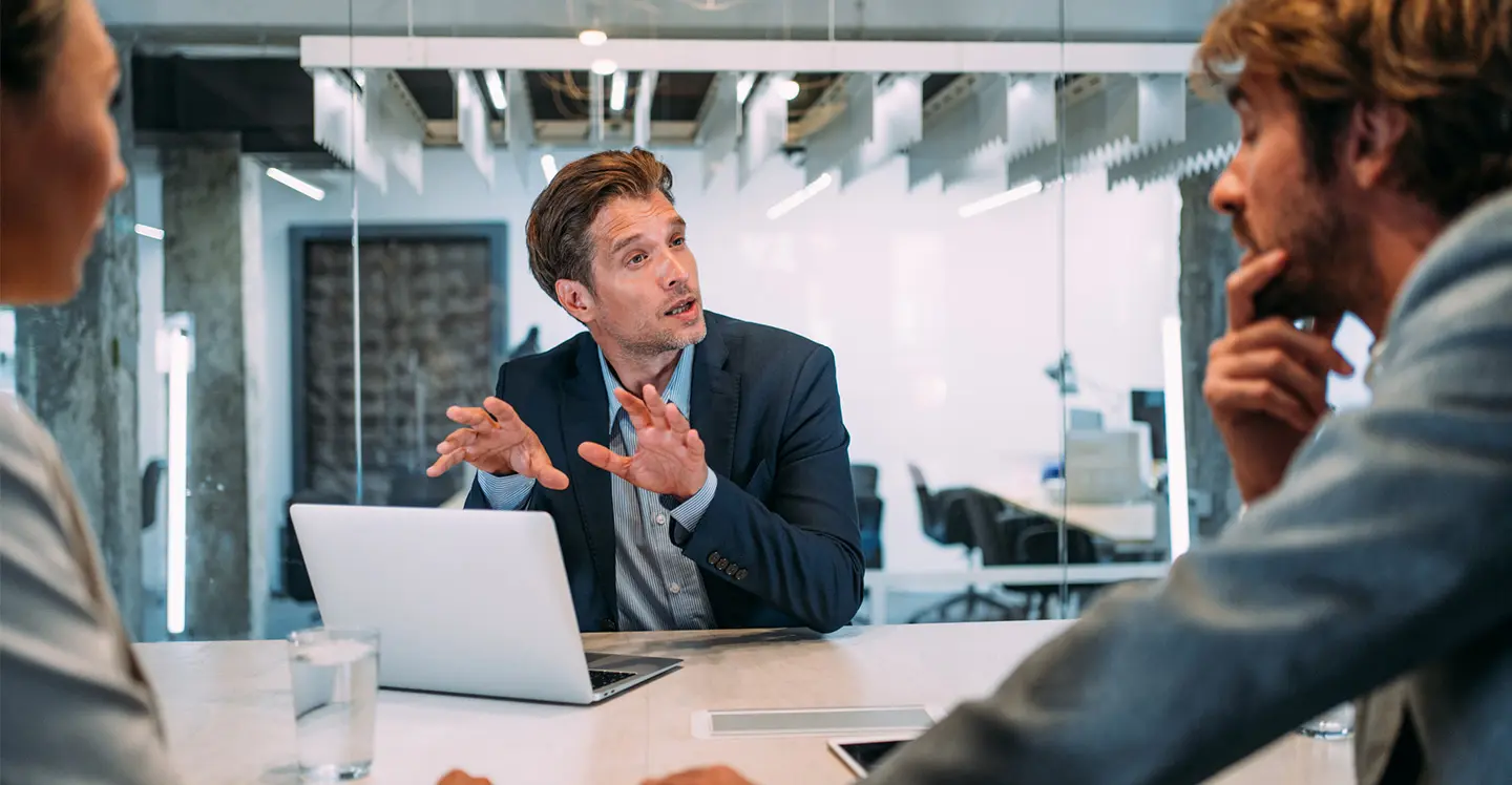 Man explains somethings to 2 attentive persons in office environment.