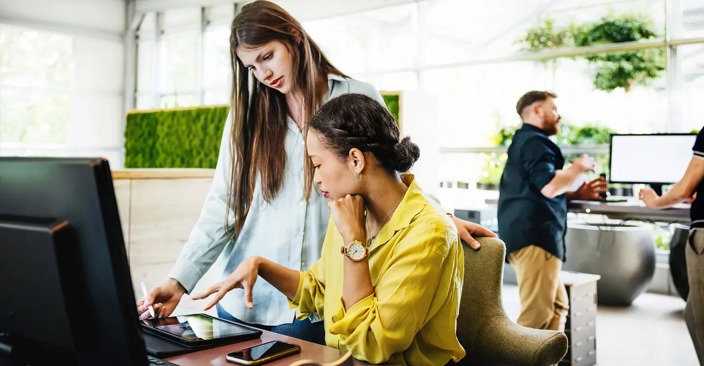 Two women looking together at something on an iPad in office environment.